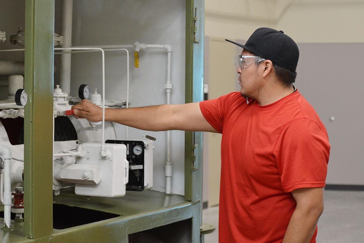 An individual wearing a hat and safety goggles turns the valve on production machinery