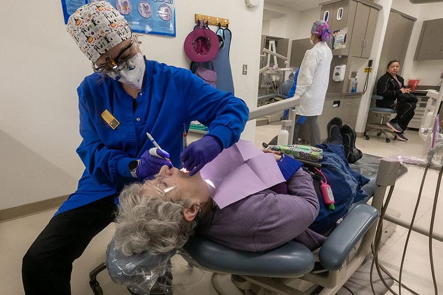 A student hygienist examines the mouth of a woman laying in a dental chair